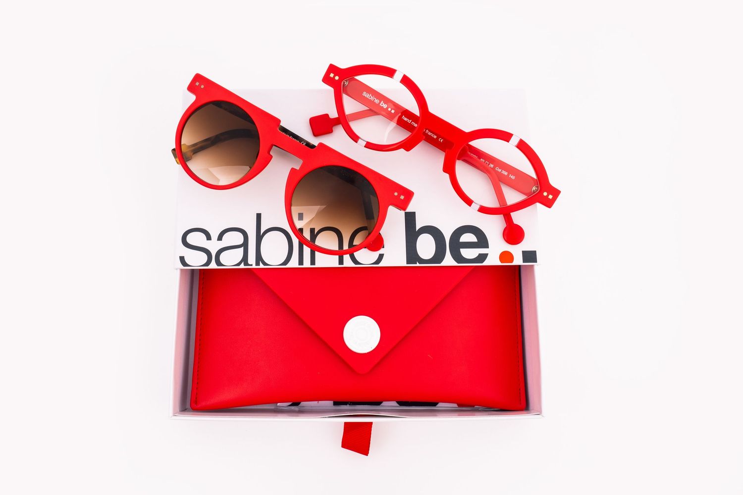 Red sunglasses and eyeglasses with a matching red case display modern optical accessories against white background.