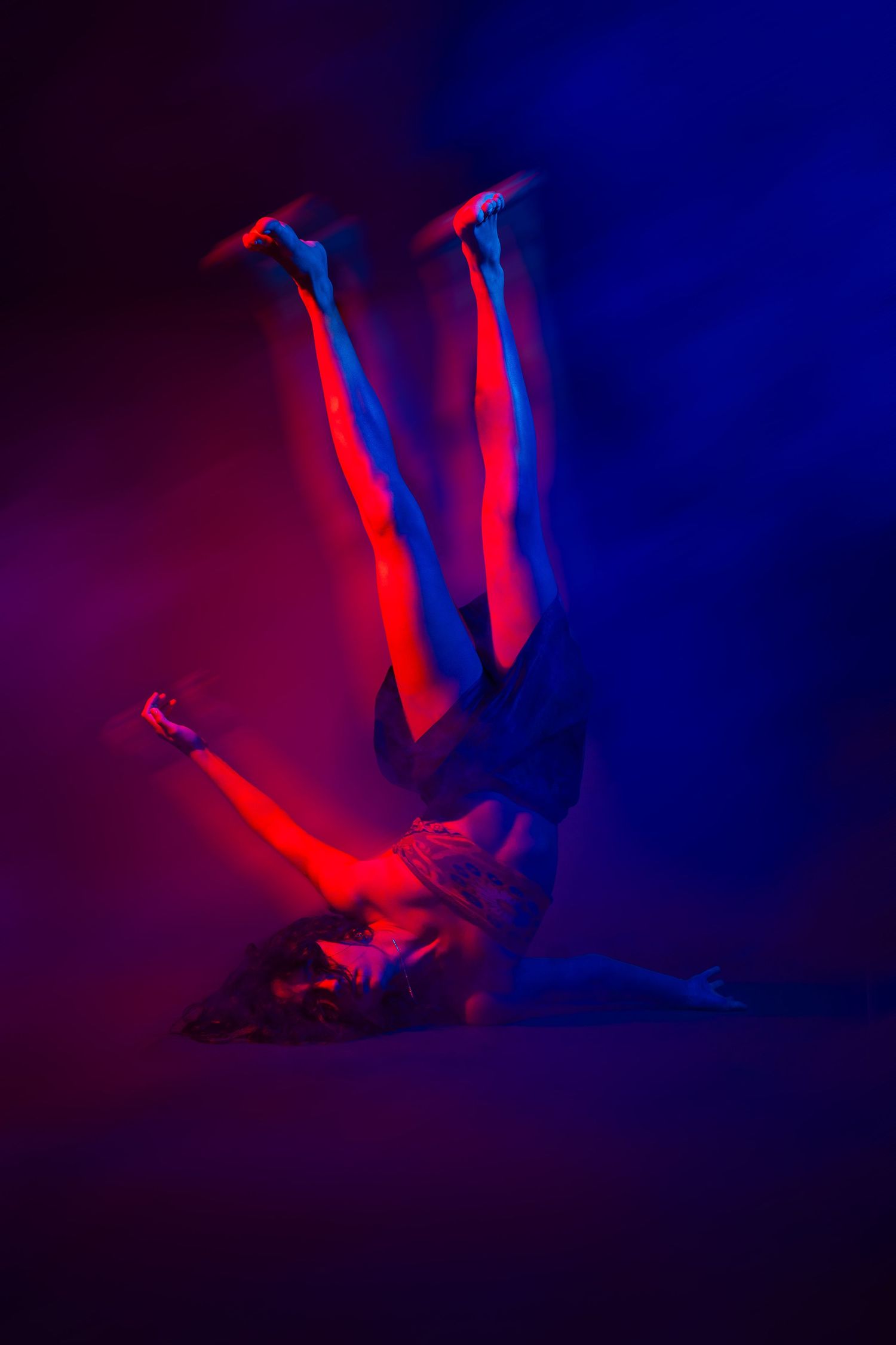 Aerial performer in vibrant red silk ribbons suspended against dark blue background with dramatic lighting effects. Vacaville Photographer,