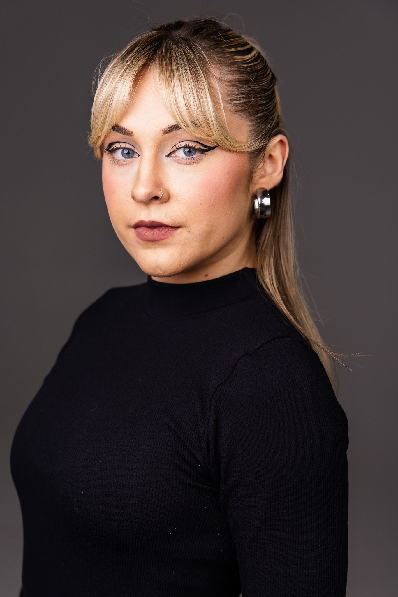 Portrait of a person wearing a black turtleneck sweater and silver earrings against a dark background.
