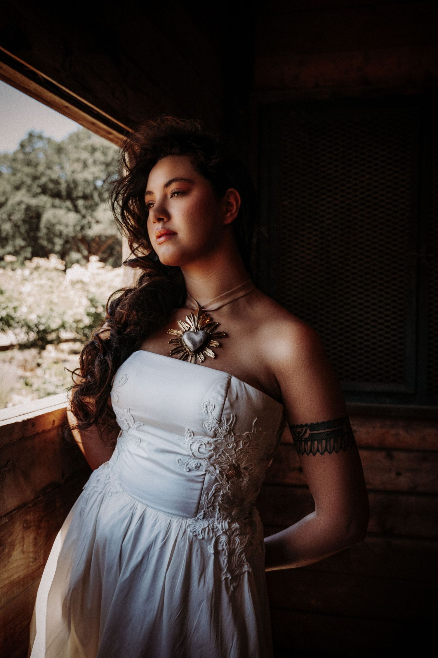 Moody portrait of a person wearing a white lace dress and statement necklace in dreamy natural lighting.