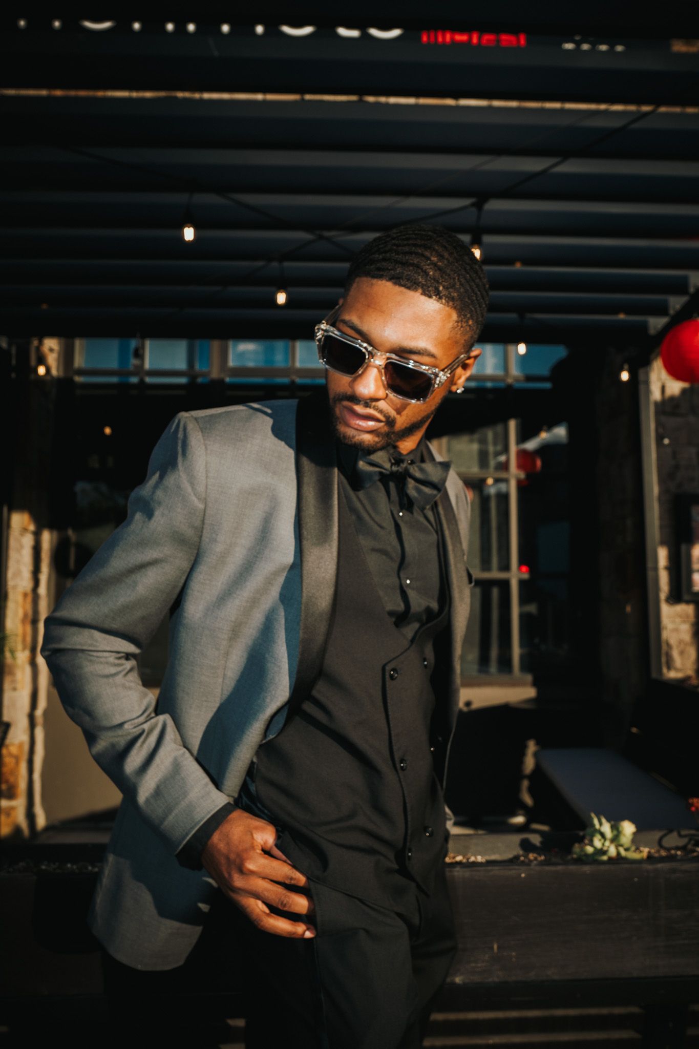 A stylish portrait of someone wearing sunglasses and a gray blazer posing confidently on a city street at sunset.