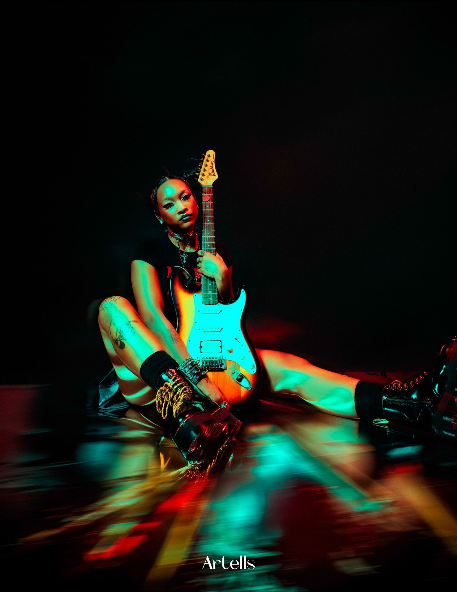 Musician in bold lighting poses with blue electric guitar against dark background with colorful neon lighting effects.