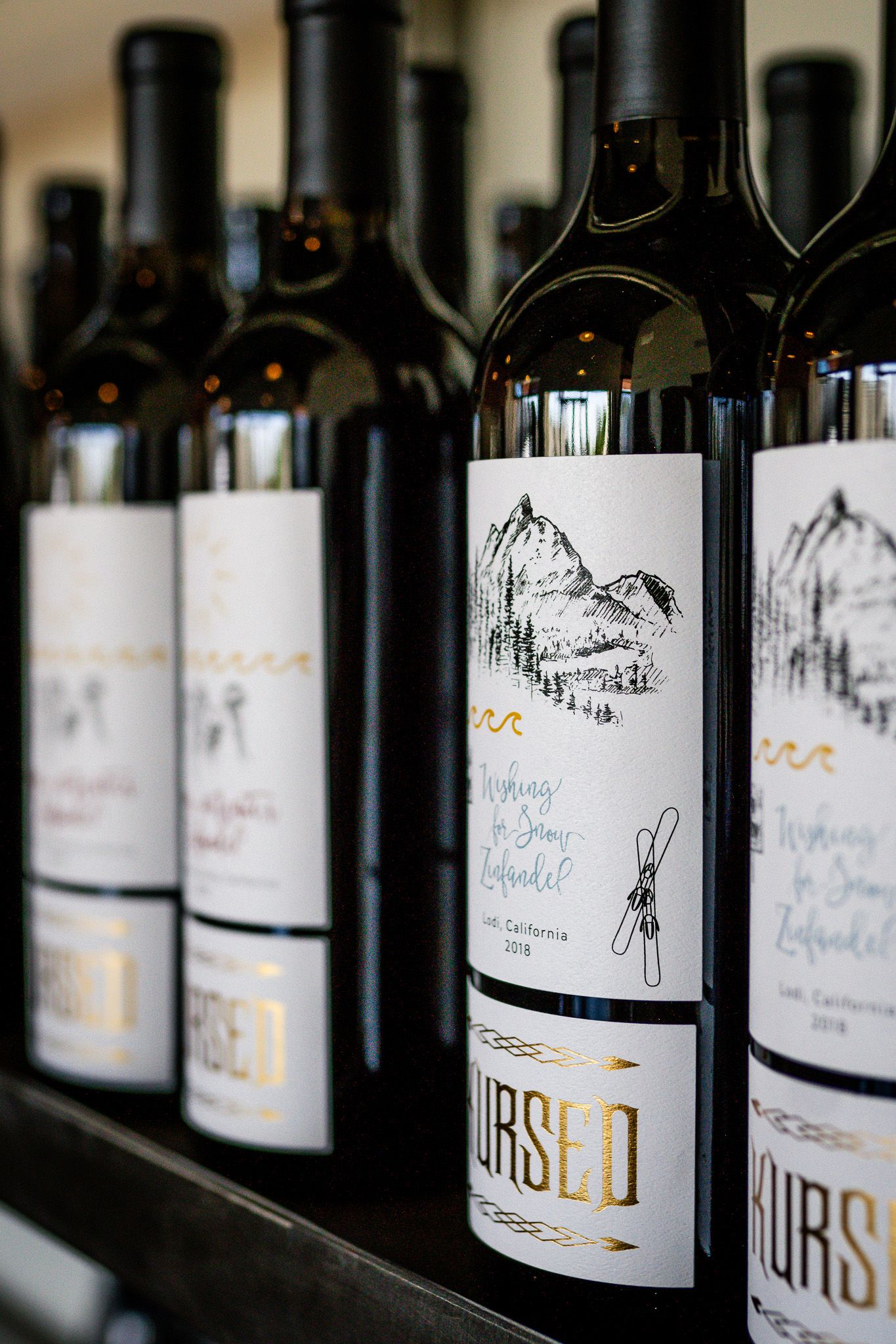 Closeup of wine bottles with artistic black and white sketch labels showing mountain landscapes on display.