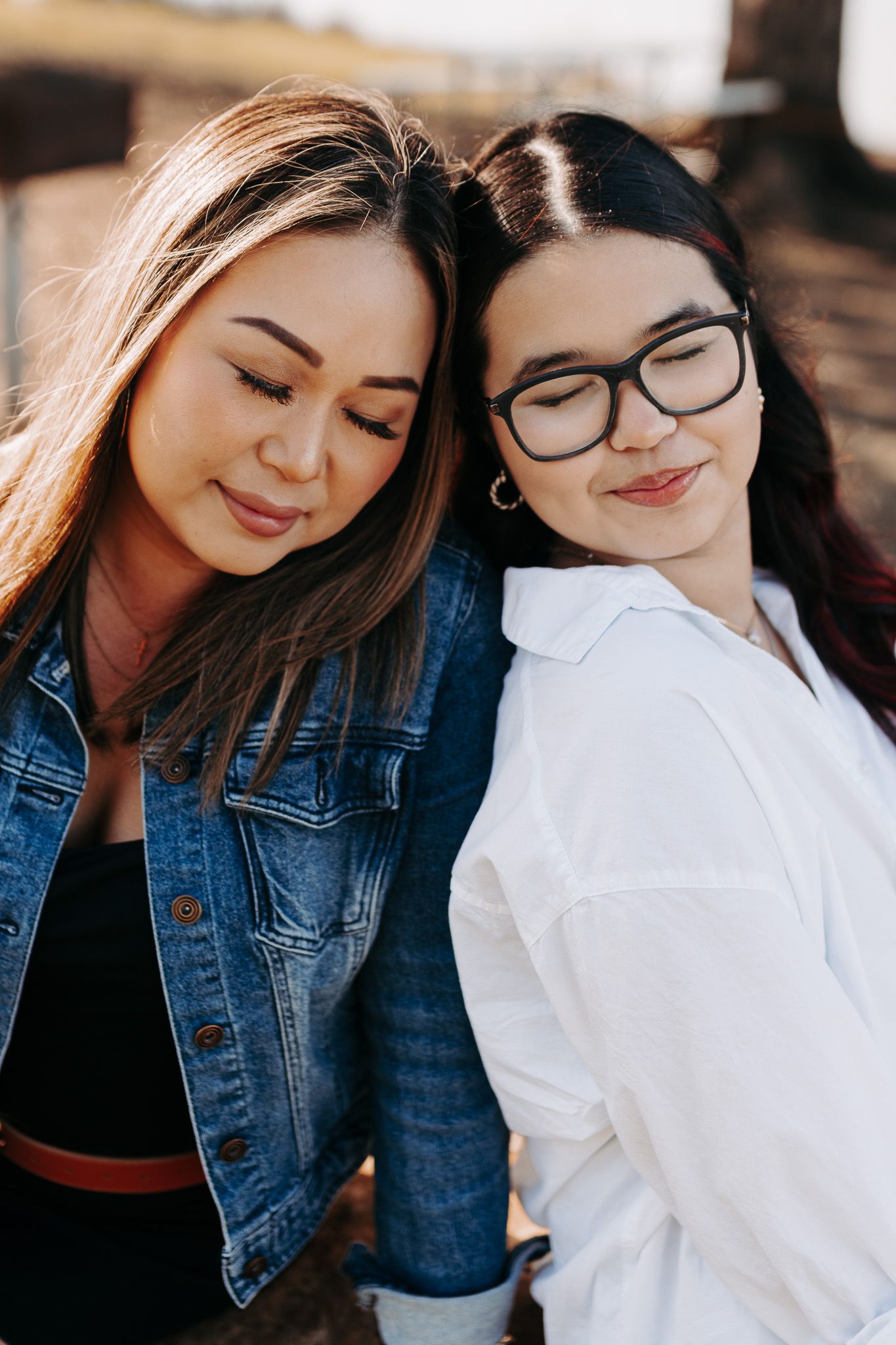 Two friends sharing a joyful moment together outdoors, one wearing a denim jacket and one in a white shirt.