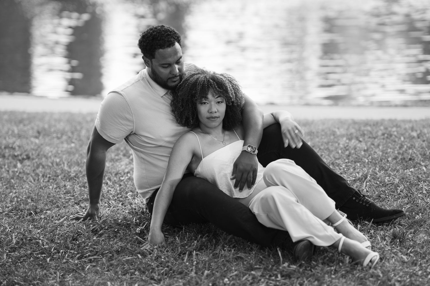 A romantic black and white portrait of a couple relaxing together on grass by a lake.