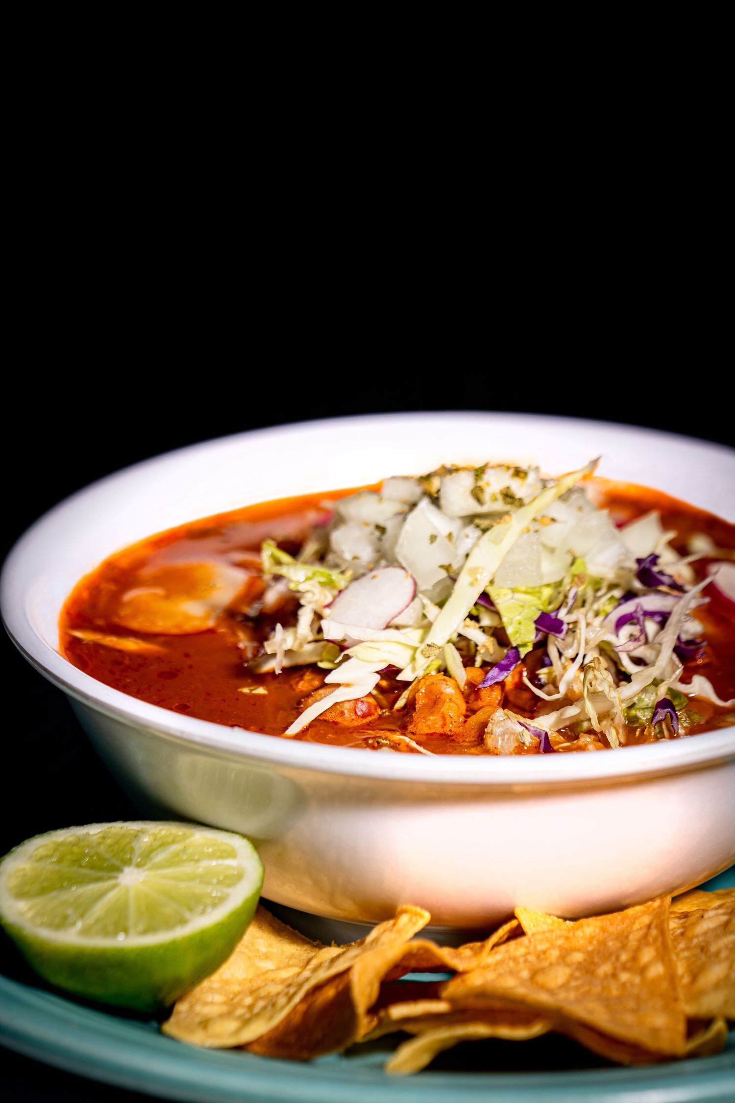 Close-up sequence of bowls filled with vibrant red tortilla soup garnished with cheese, lime, and crispy tortilla strips.