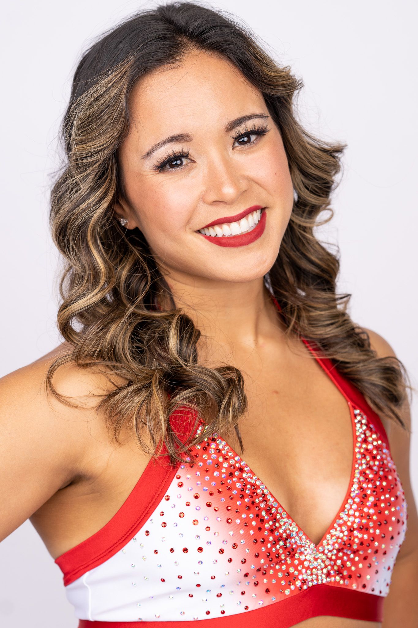 Portrait in red and white sparkly performance costume with styled wavy caramel highlighted hair and bright red lipstick.
