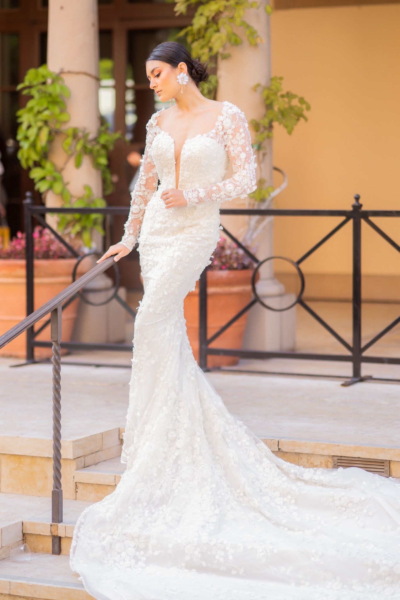 Elegant lace wedding gown with long sleeves and flowing train on a model posing on outdoor steps.