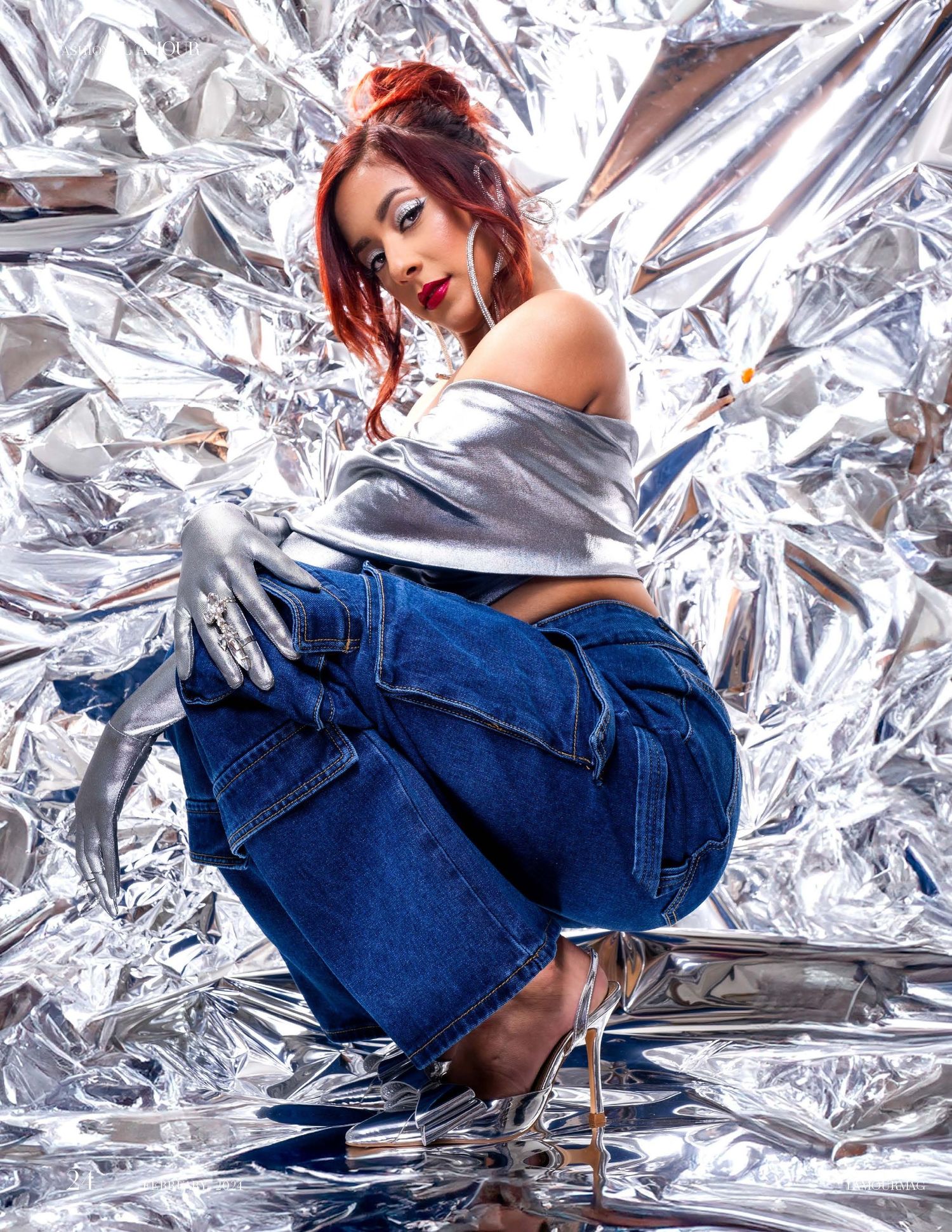 Fashion photo against metallic silver foil backdrop features model in off-shoulder top and baggy jeans with heels.