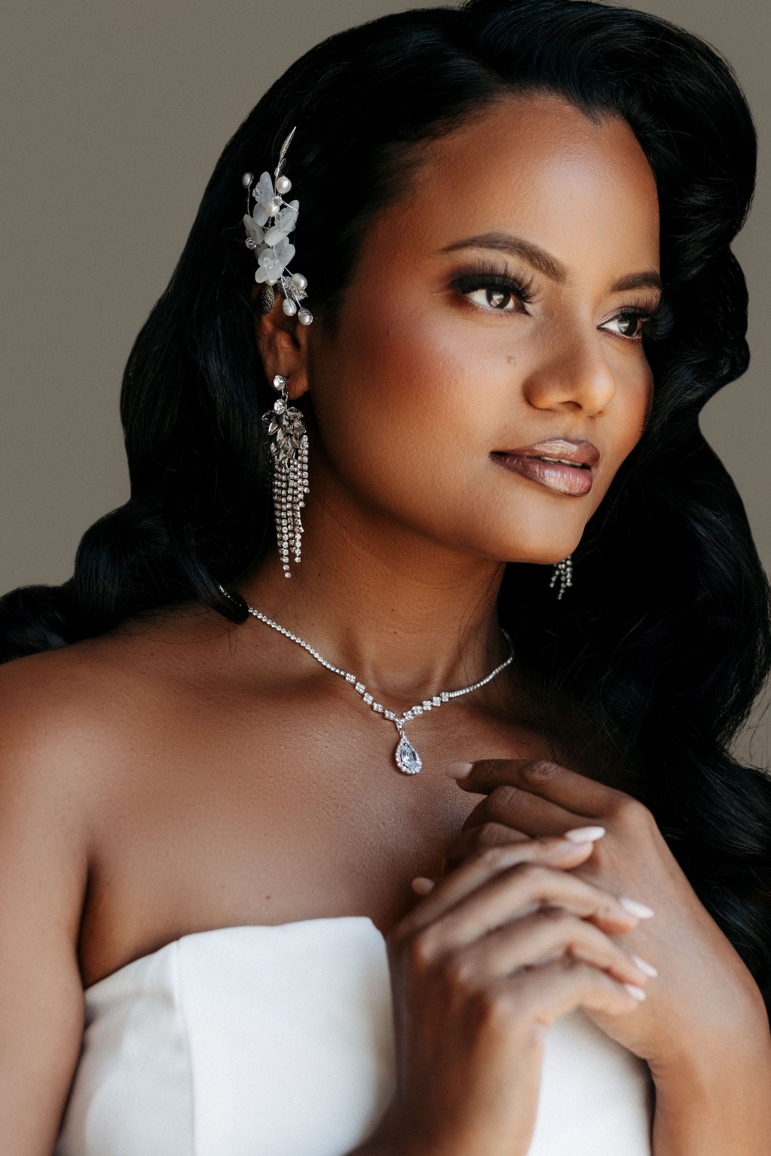 Elegant bridal portrait featuring sparkling diamond jewelry, floral hair accessories and a white strapless gown.