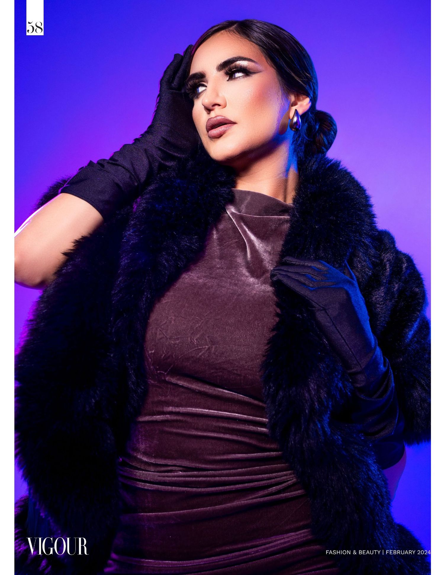 Fashion model in brown velvet dress and dark fur coat poses dramatically against vibrant purple backdrop with glamorous makeup.