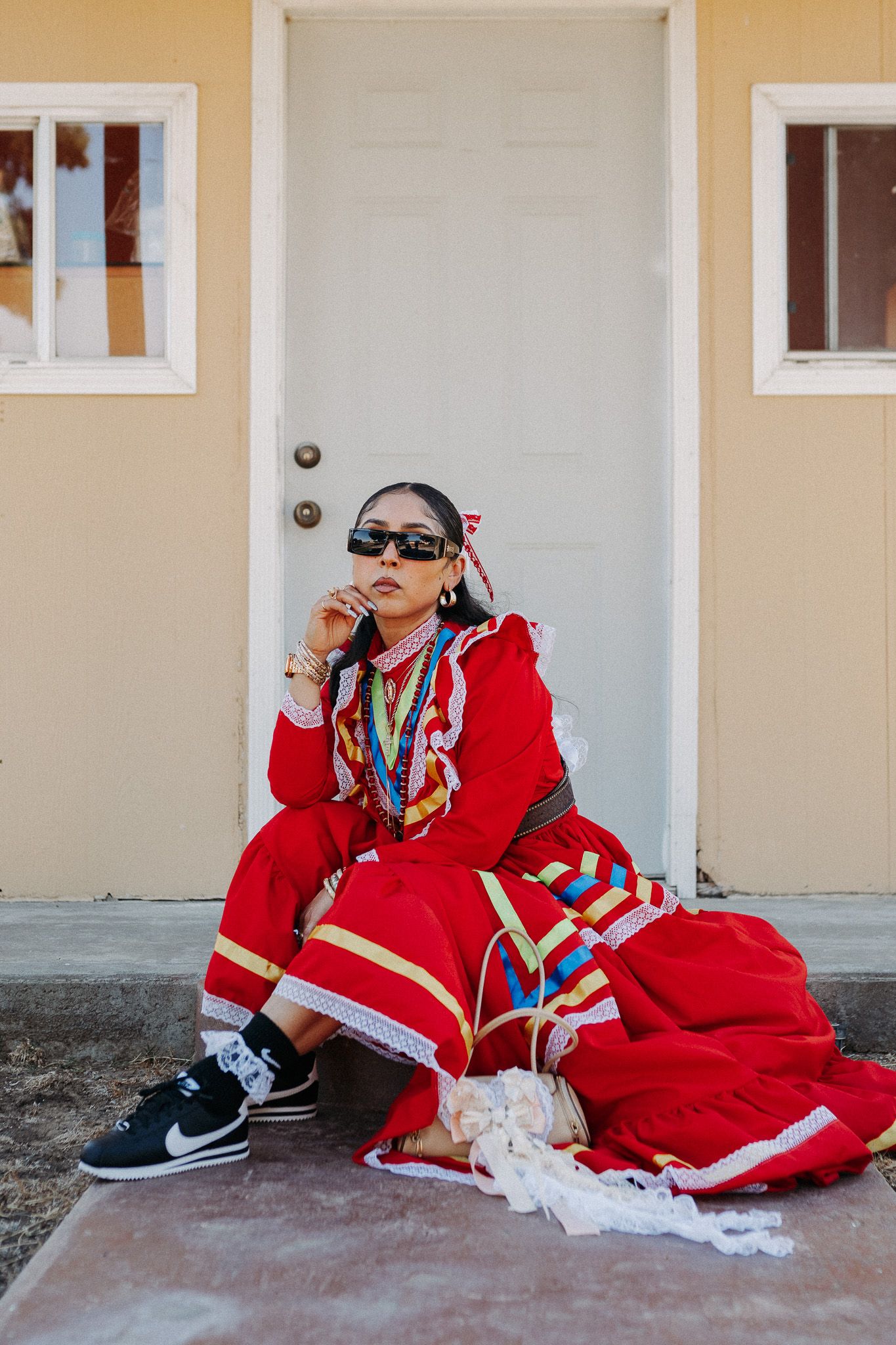 Street fashion portrait in a bright red traditional dress with sneakers and colorful accessories against white door.