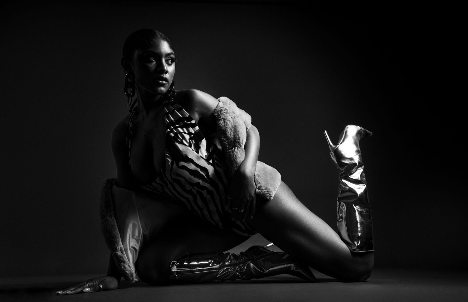 Black and white artistic portrait of a person seated in dramatic lighting with a spotlight on the floor.