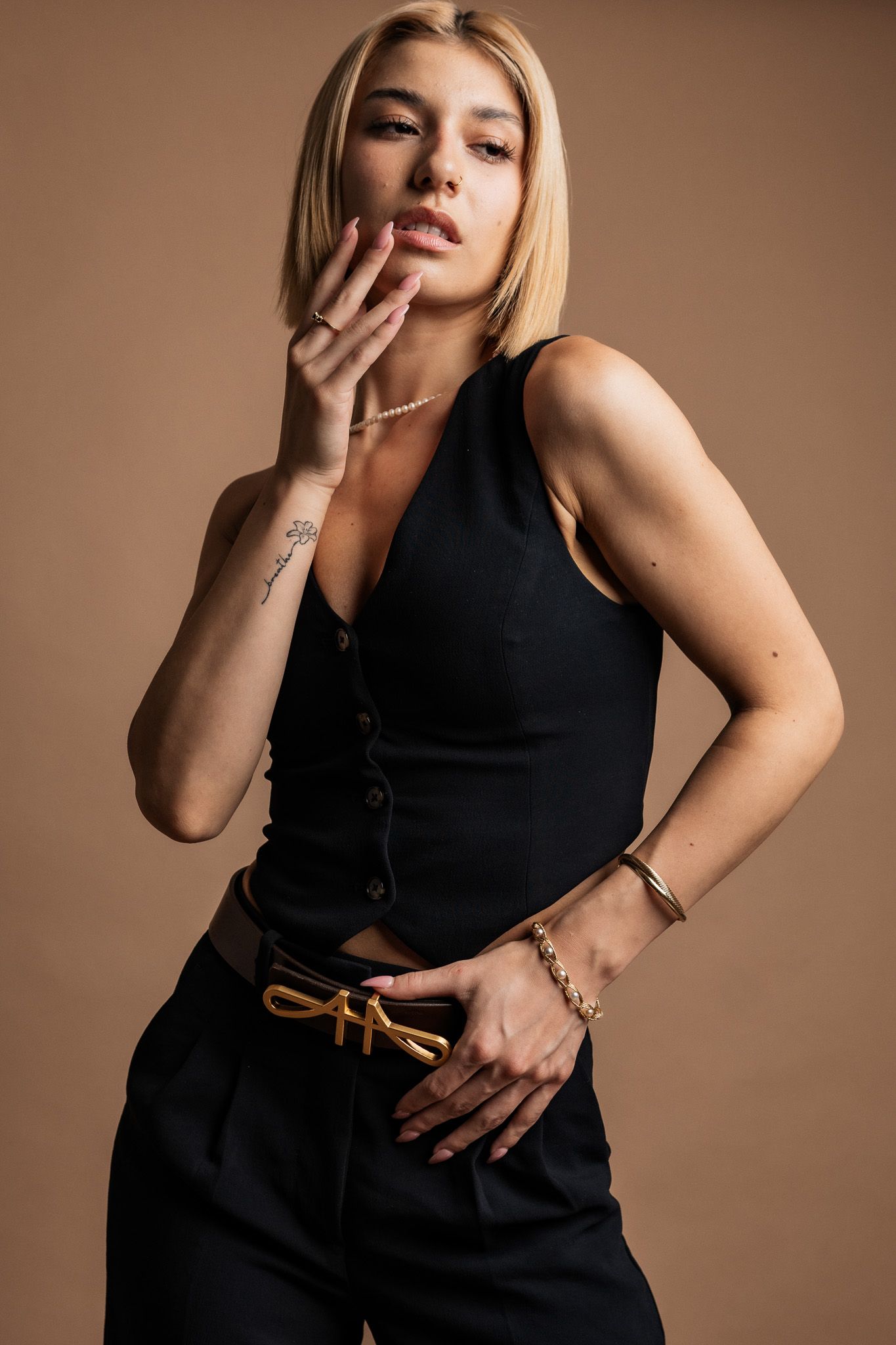 Fashion portrait of person in black sleeveless top posing against brown background with delicate hand gestures.