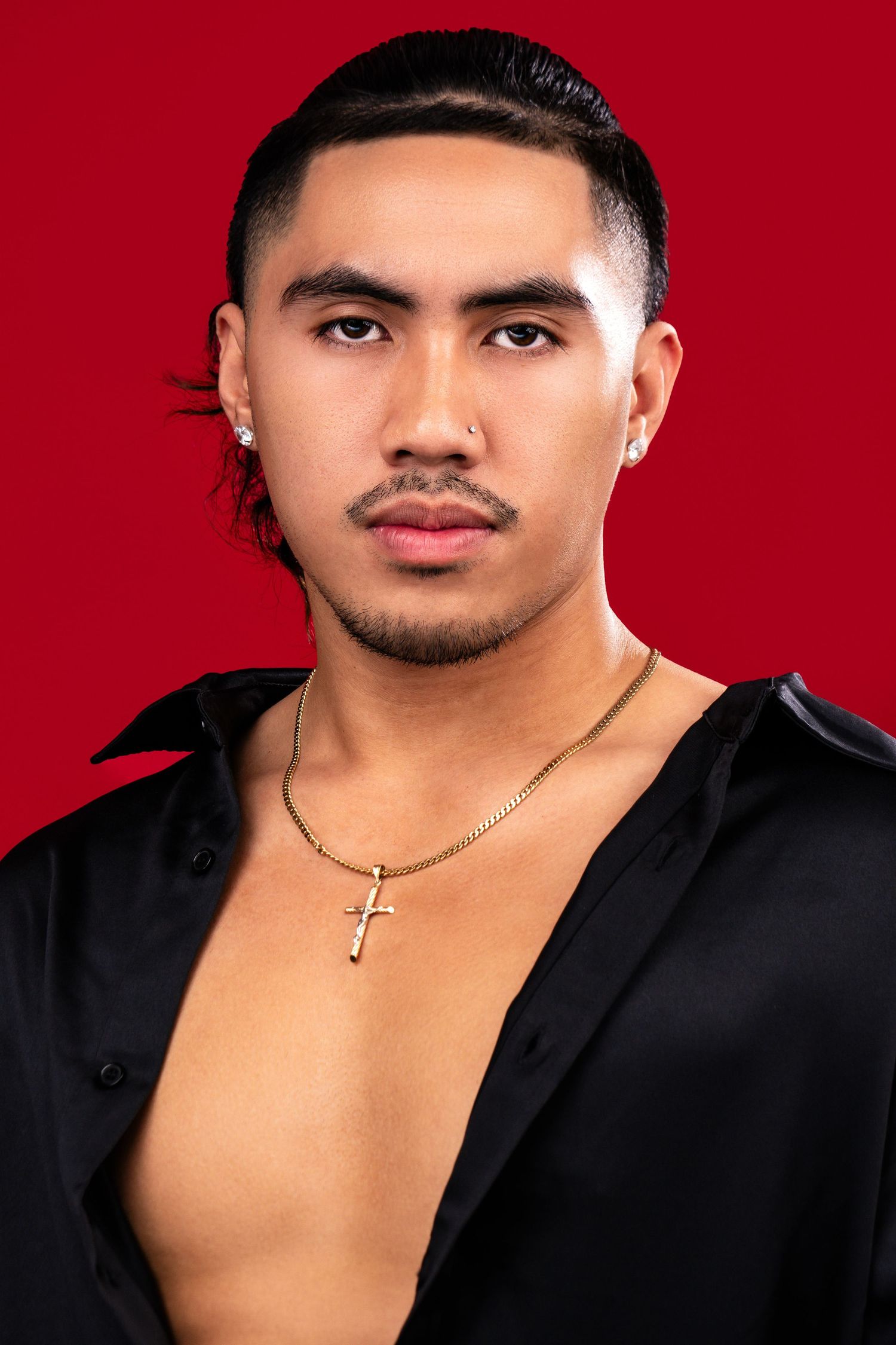Portrait of an Asian man wearing a black open shirt and cross necklace against a red background.
