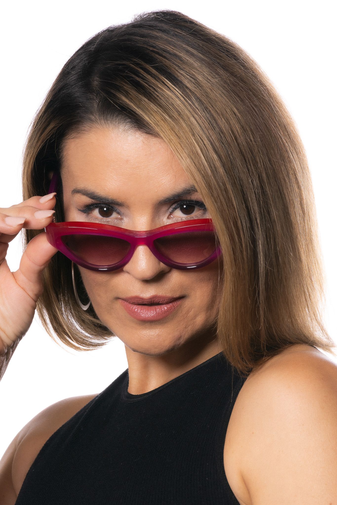 Glamorous portrait of a person wearing sleek red sunglasses and a black sleeveless top with highlights in their brown hair.