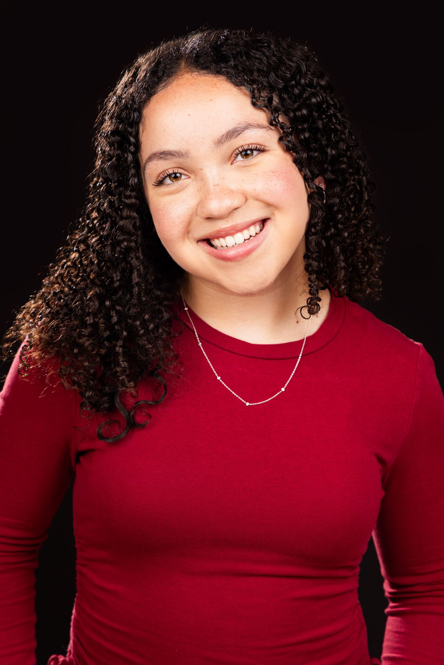 A person in a red top with curly black hair poses against a dark background in a series of studio photos.