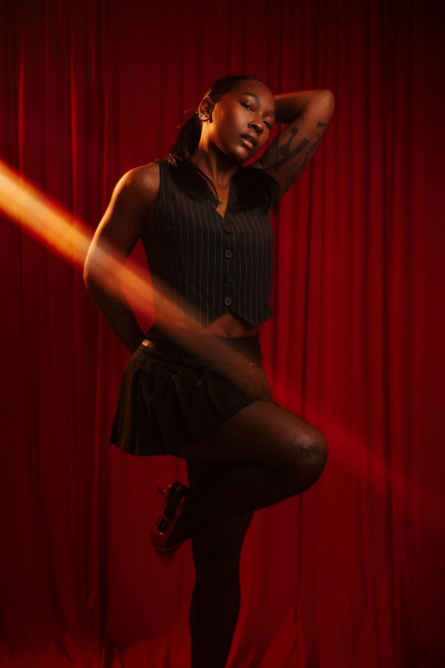 A dancer in a black outfit strikes a dynamic pose against a red curtain backdrop with dramatic lighting effects.