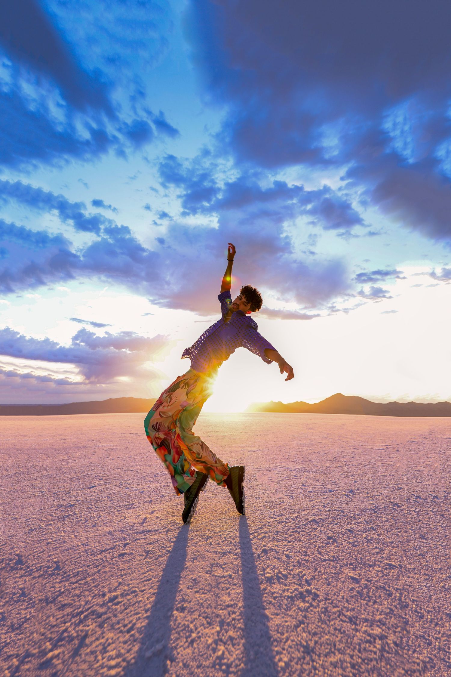 Silhouette of person leaping joyfully on salt flats during dramatic sunset with purple clouds and mountains.