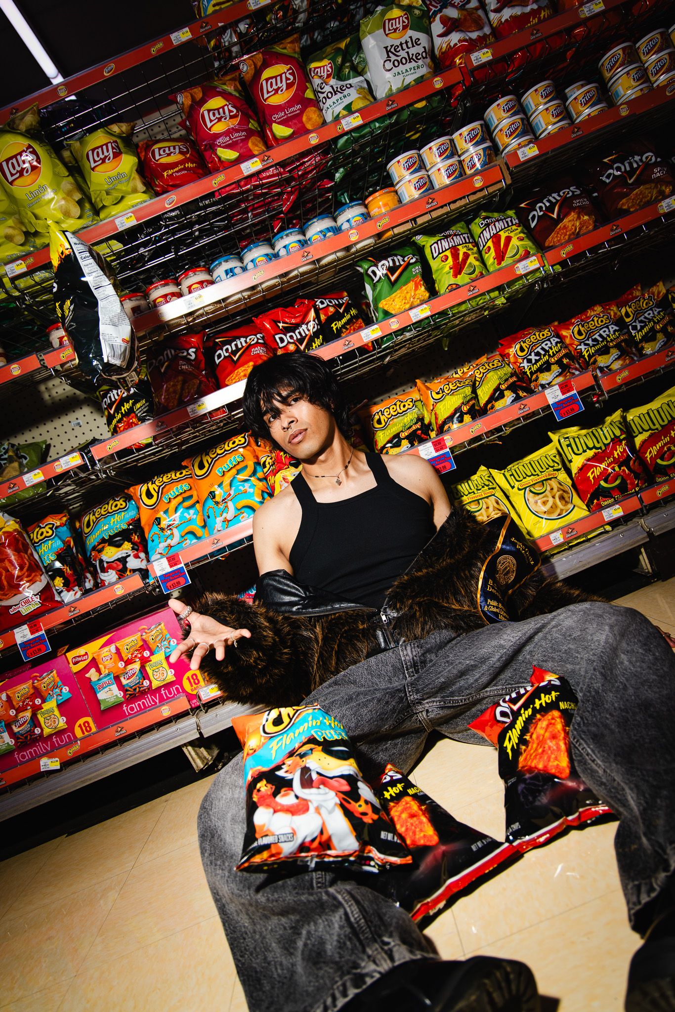 Moody shot in snack aisle showing opened bags of chips scattered on floor with convenience store shelves in background.