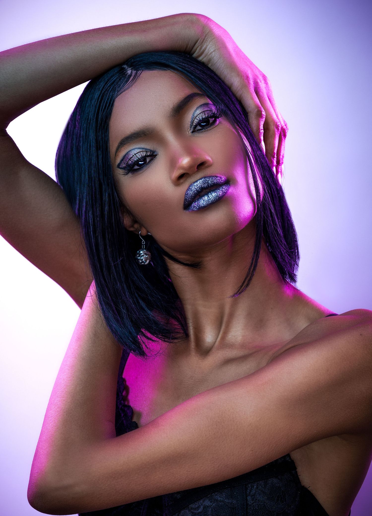 Glamorous beauty portrait with glitter makeup and shimmering lips in purple and pink lighting against dark background.