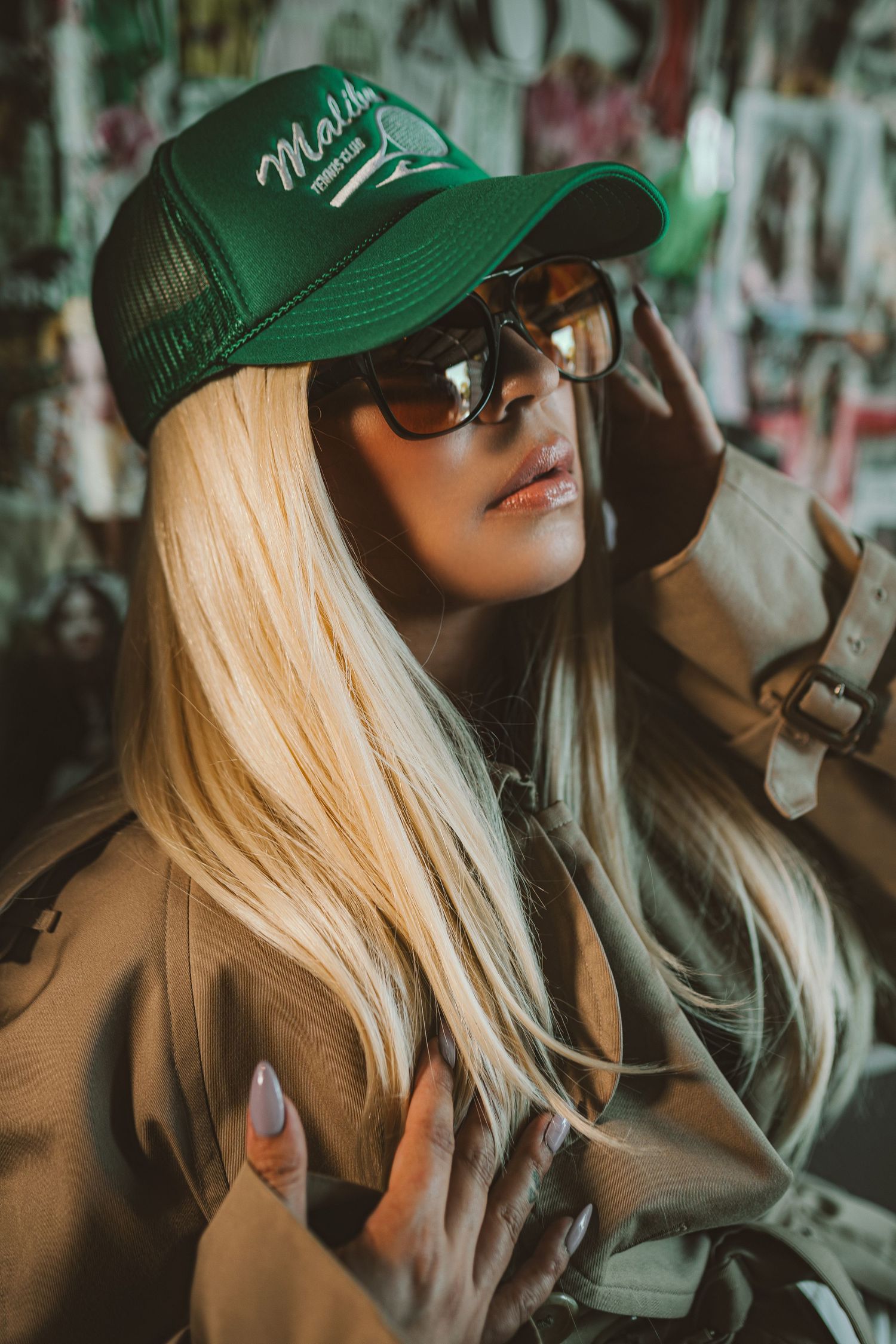 Long blonde hair with green trucker cap and sunglasses photographed against graffiti wall in cinematic style.