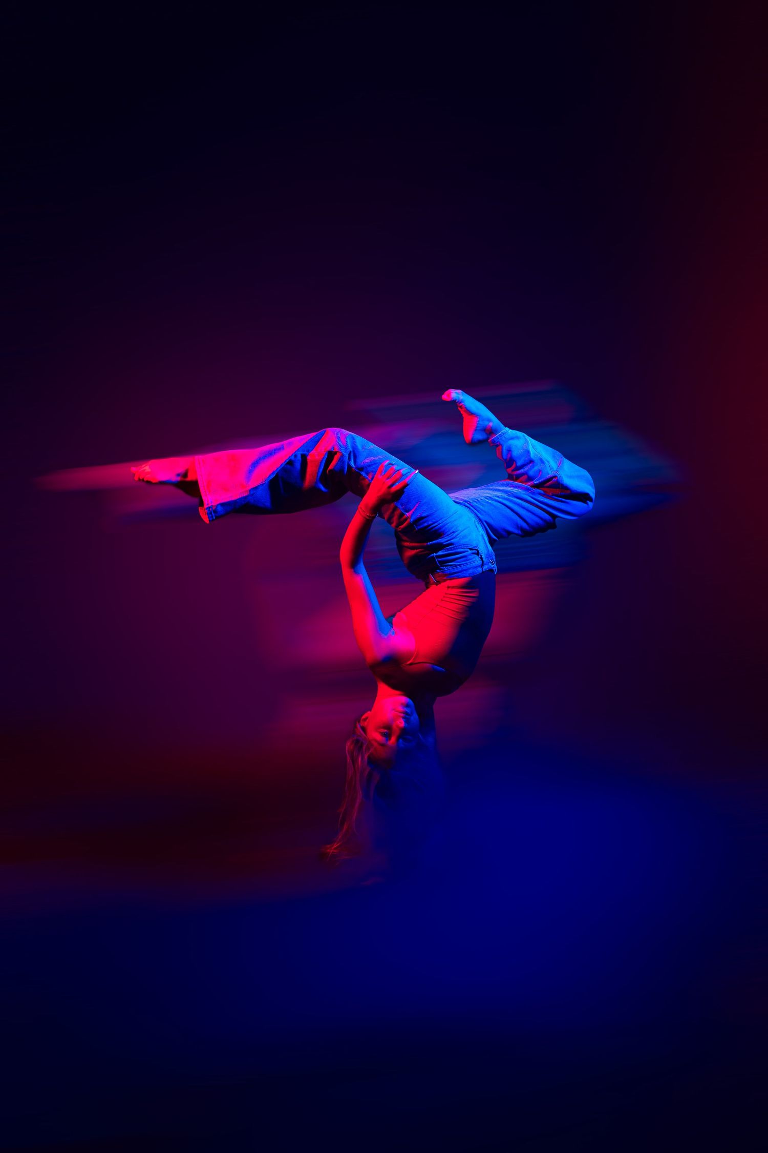 Dancer in dramatic pose illuminated by vibrant red and blue lighting against dark background creating artistic silhouette.