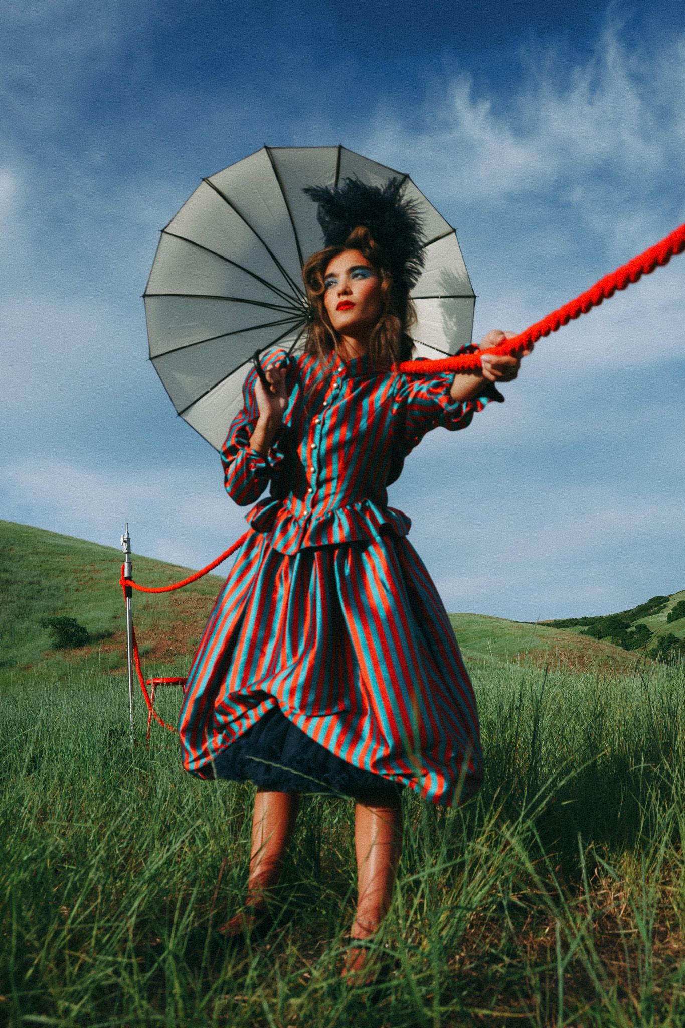 Artistic fashion photo of someone in a striped vintage dress holding a parasol in a grassy field.
