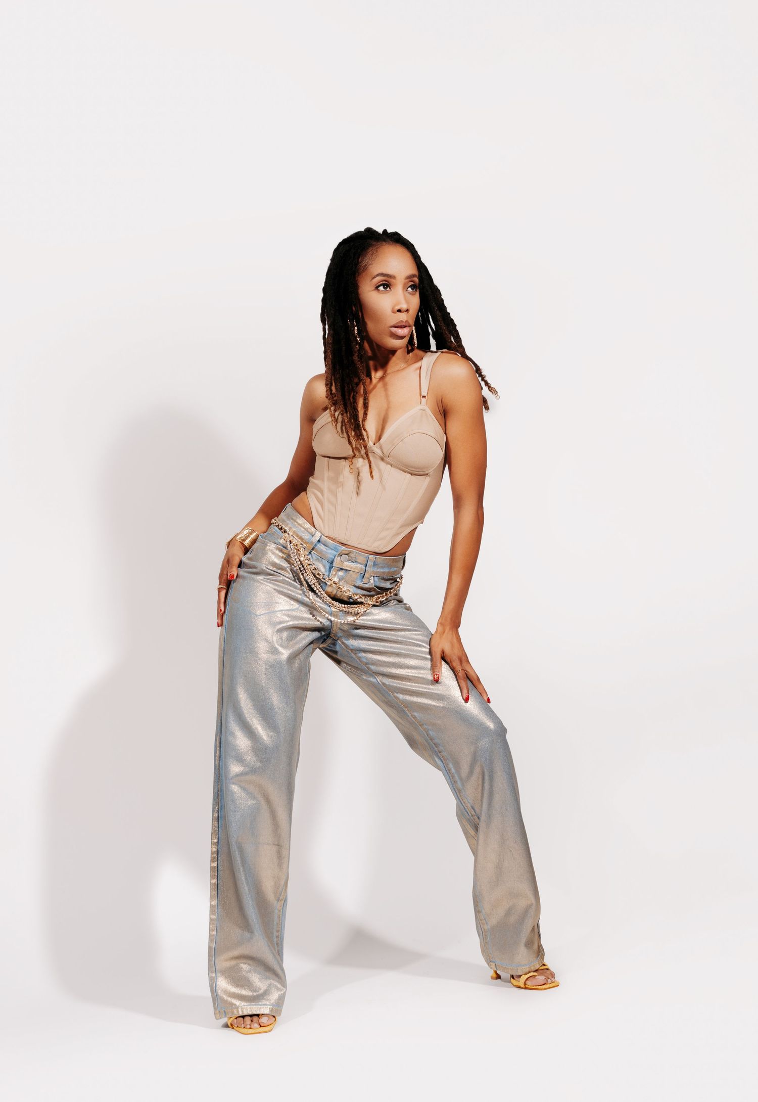A person in a beige bodysuit and metallic silver pants poses against a white background.
