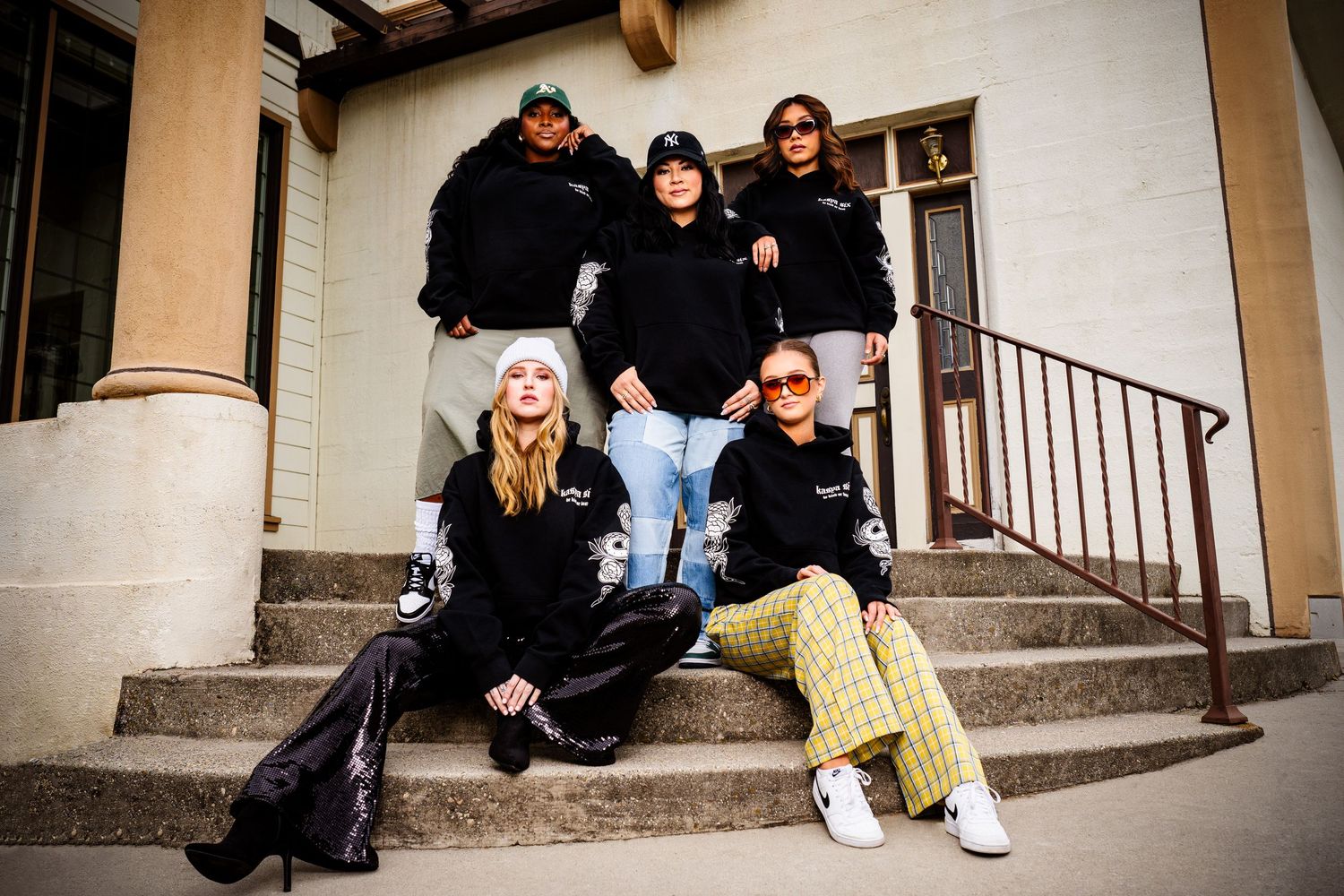 Five people in dark clothing sit casually on concrete steps outside a building.