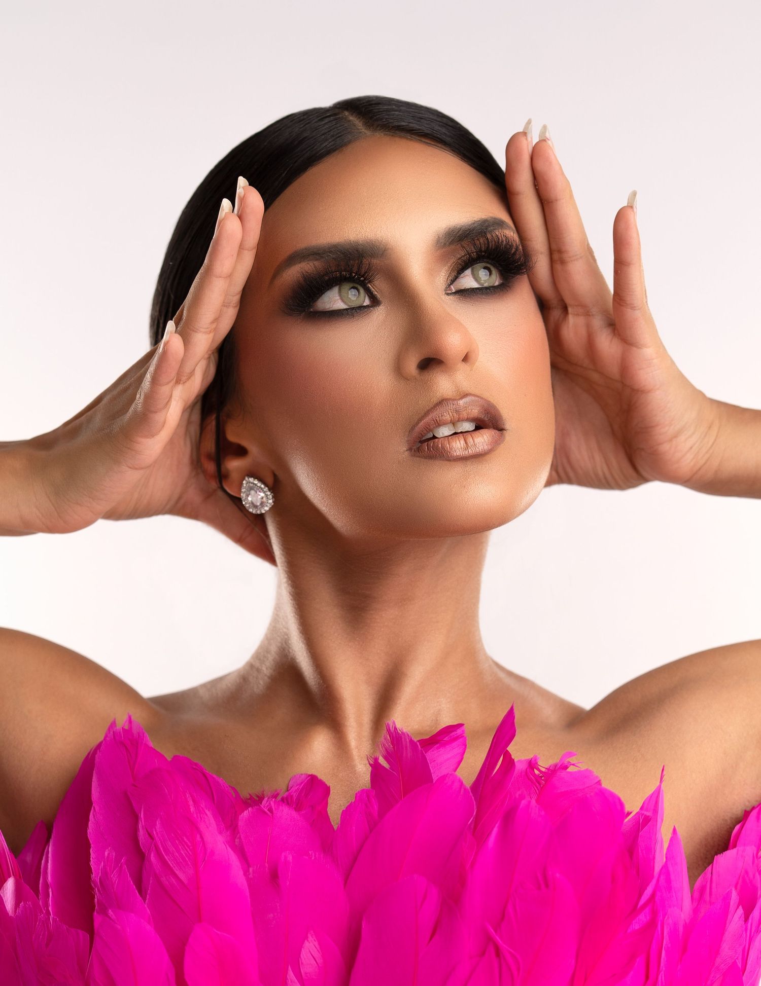 Beauty photo featuring dramatic glam makeup, glamorous styling and vibrant hot pink feathers against light backdrop.