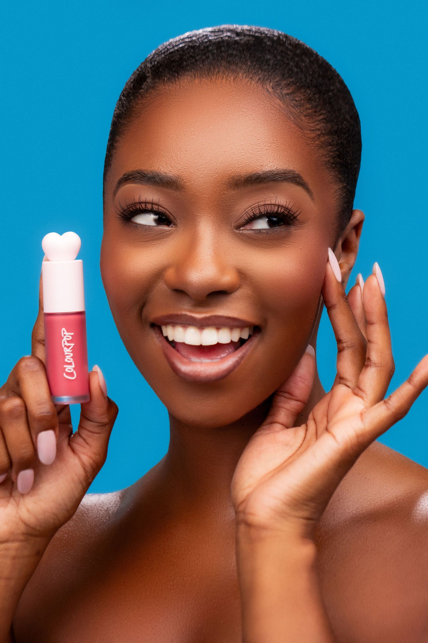 Beauty advertising photo showing a glowing model holding pink cosmetic product against bright blue background.