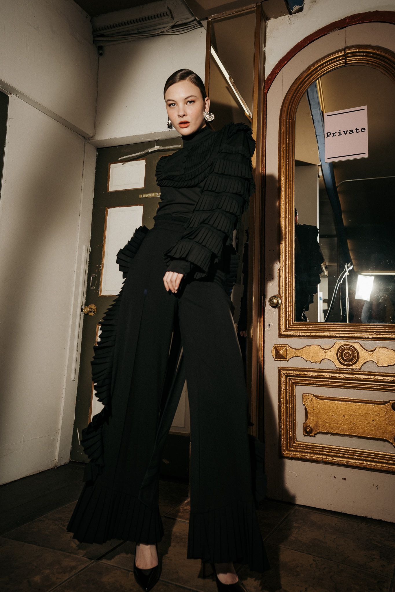 Dramatic fashion photo showing a black monochromatic outfit with ruffled turtleneck sweater and flowing wide-leg pants.