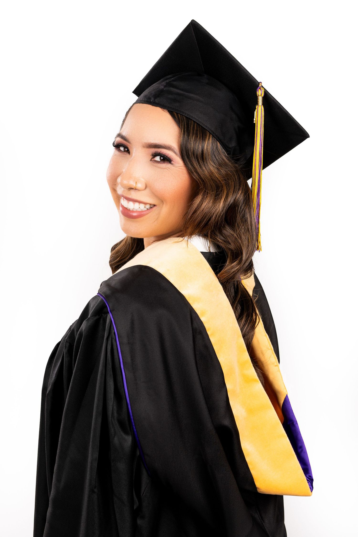 Graduate wearing black cap and gown with gold honor stash poses against white background with warm smile.