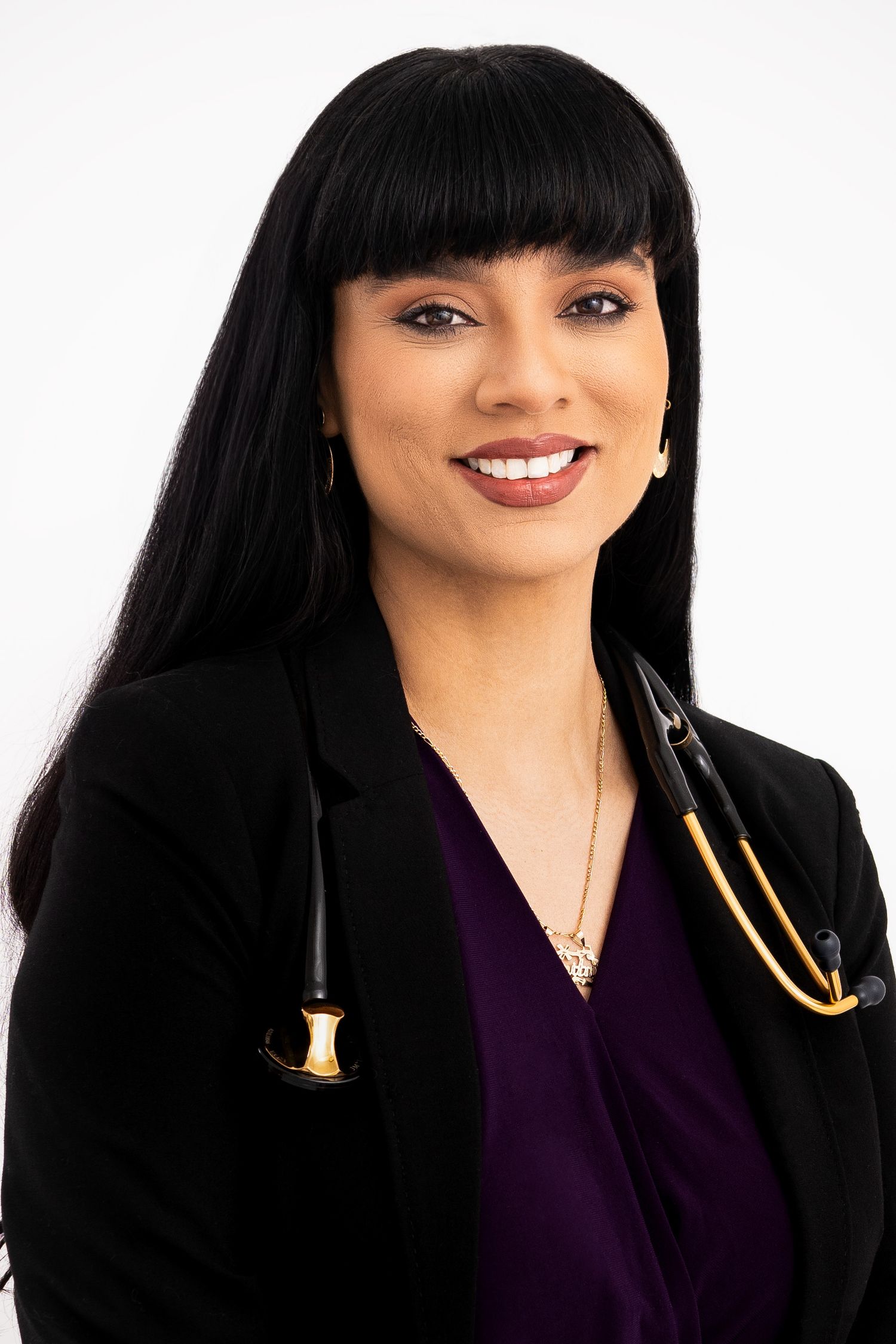 Healthcare professional wearing a black blazer and purple scrubs with a stethoscope around neck in professional headshot.