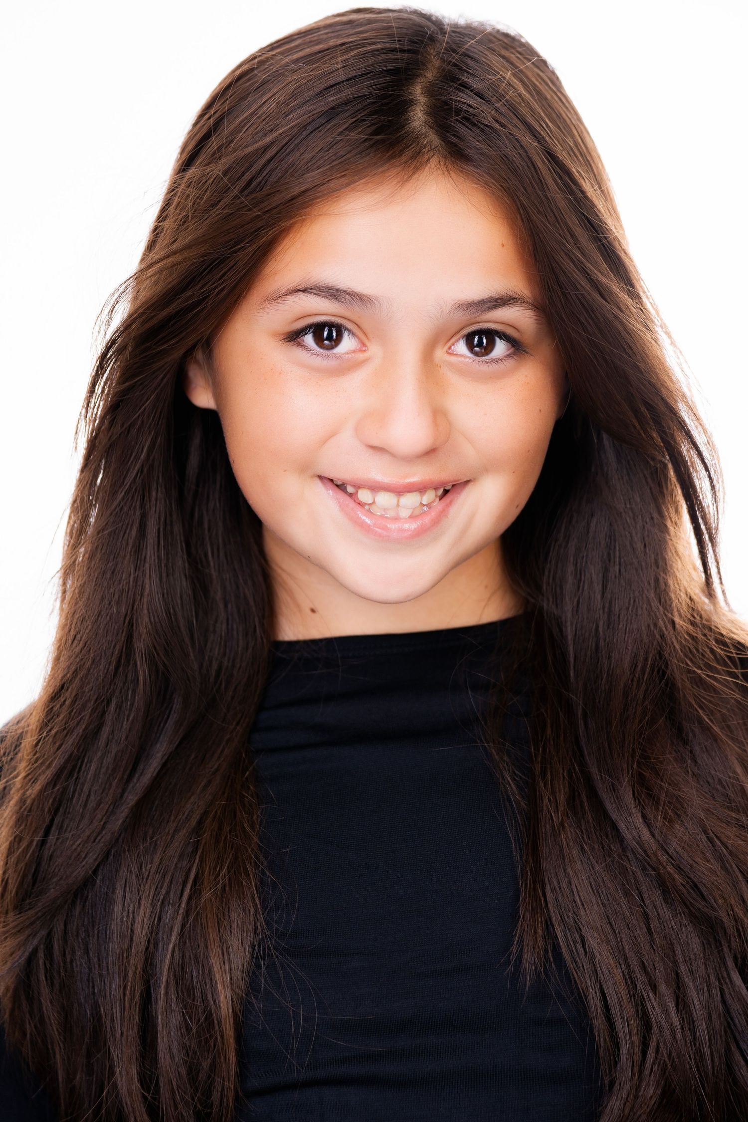 Portrait of a cheerful young person in a black top with long dark hair and a warm smile against a white backdrop.