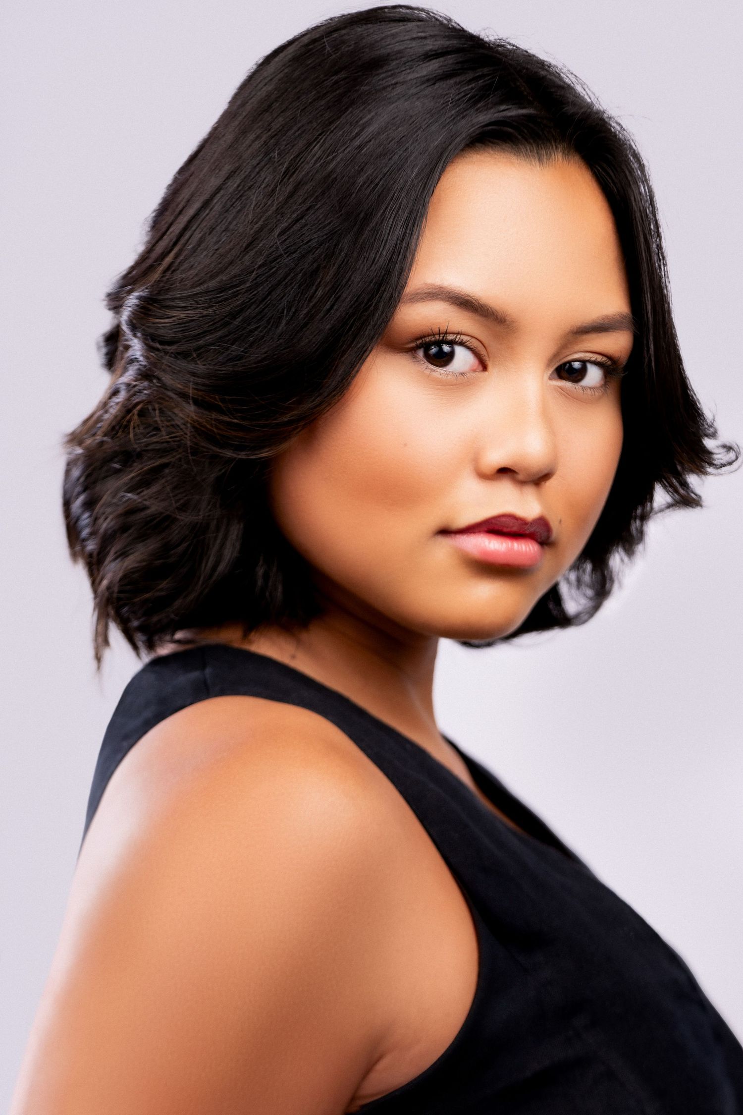 Professional studio portrait with dramatic lighting featuring a glamorous shoulder-length black hairstyle and black sleeveless top.