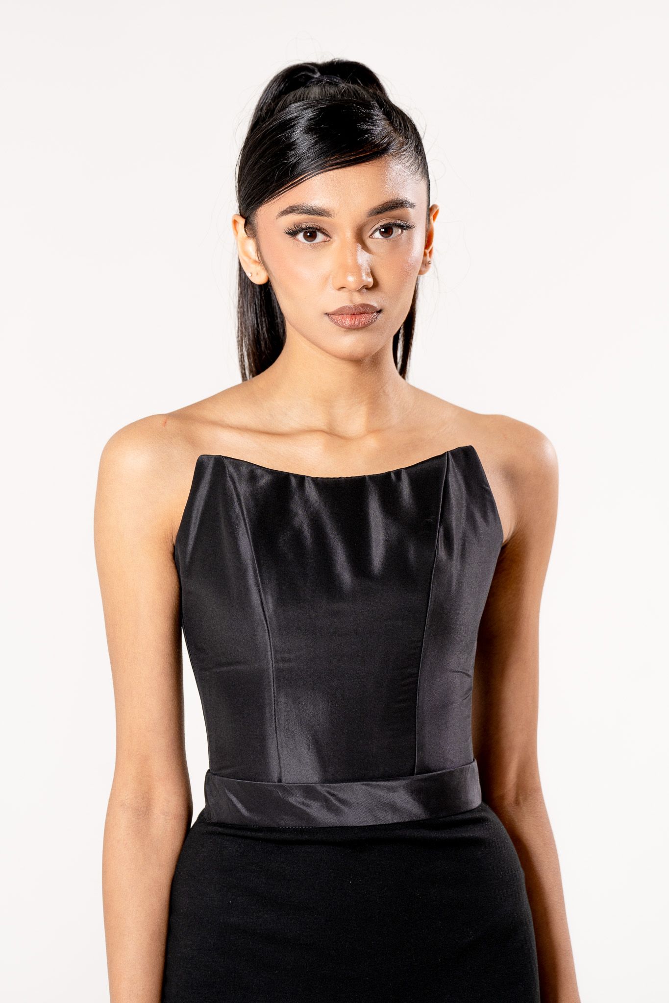 A model poses in an elegant black satin strapless bodice with sleek hair against a light backdrop.