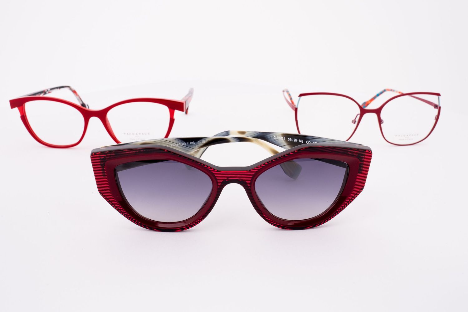 Three red eyeglass frames arranged on a white background, including a sunglasses style frame with gradient lenses.