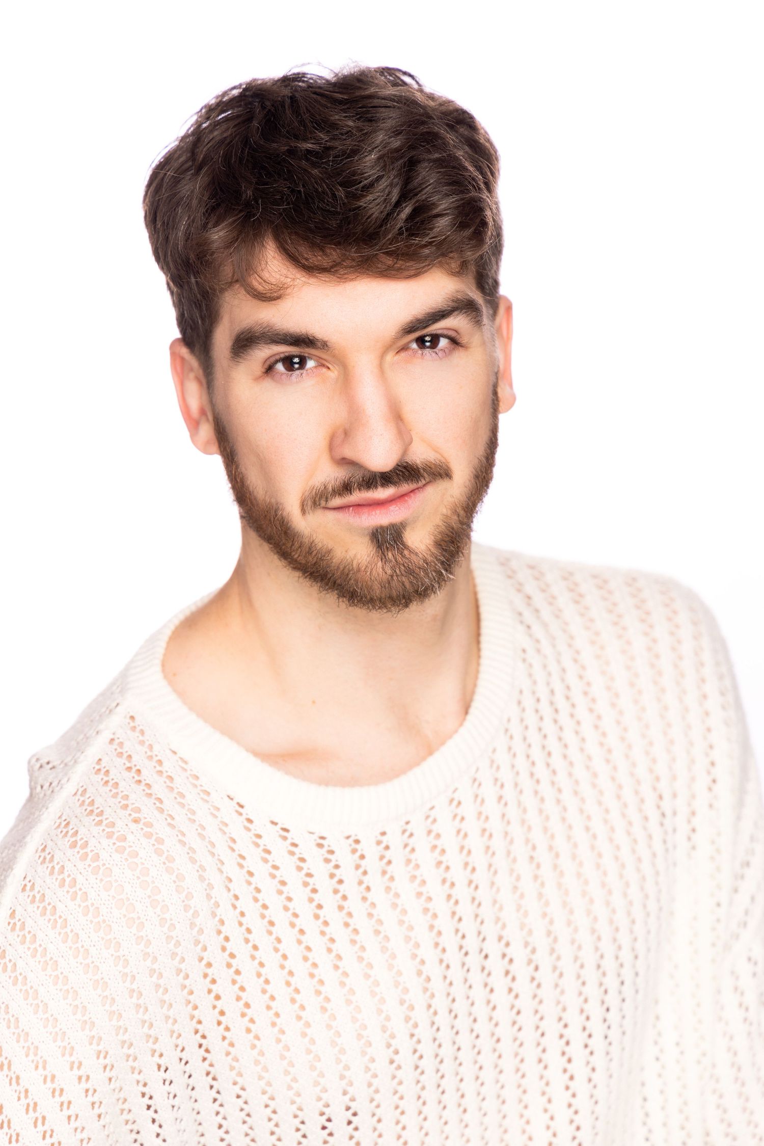 A person wearing a white knit sweater poses against a light background while smiling warmly at the camera.