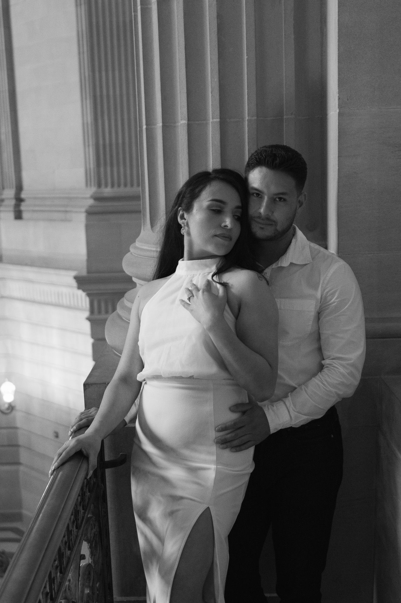 A romantic black and white portrait of a couple embracing near elegant marble columns.