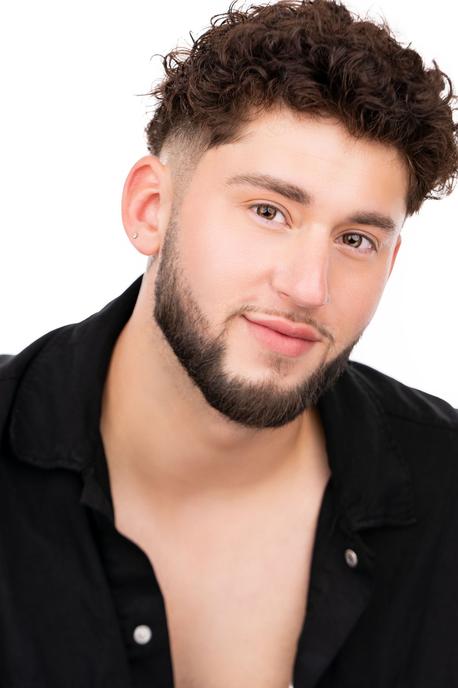 Portrait of someone with curly dark hair wearing an unbuttoned black shirt against white background.
