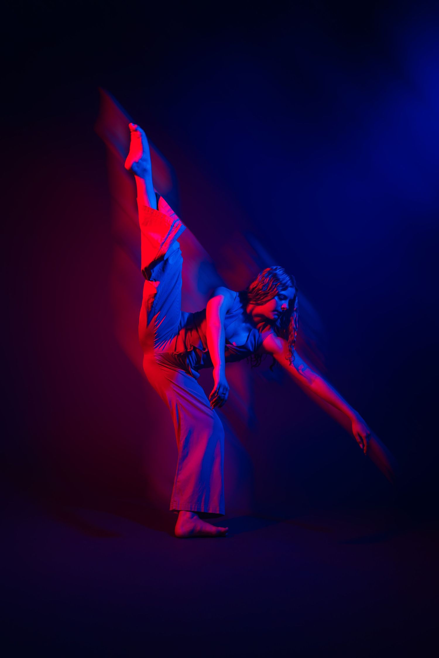 Contemporary dancer in fluid motion captured under vibrant red and blue stage lighting.