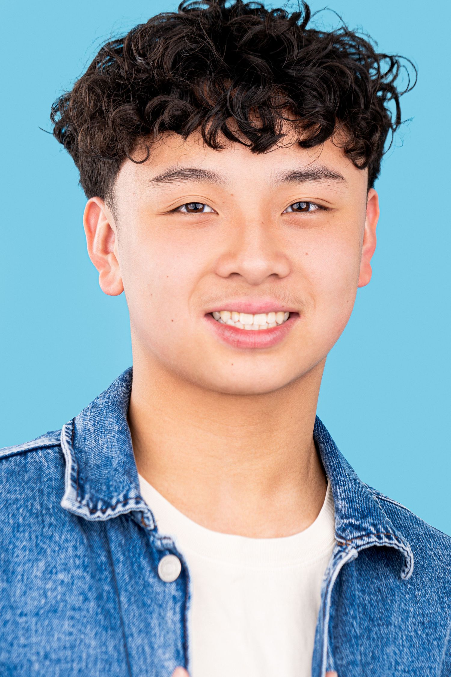 Portrait photo of a smiling person wearing a denim jacket and white shirt against a light blue background.