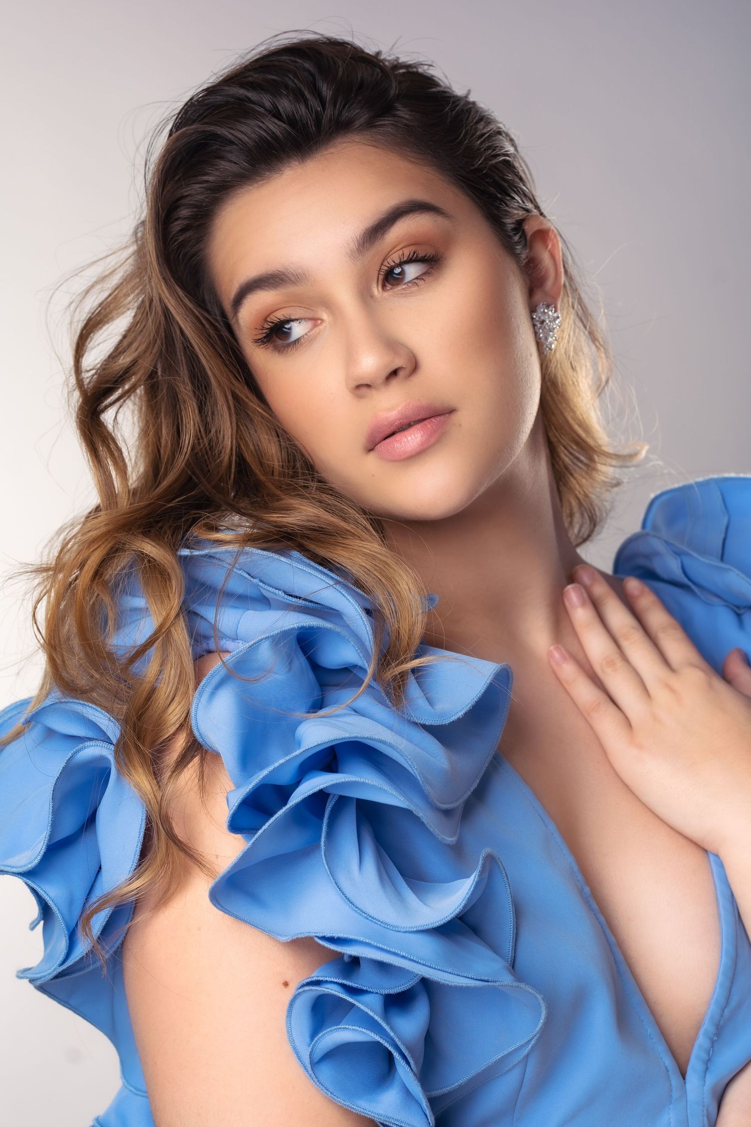 Fashion portrait with dramatic light blue ruffled top and ombre wavy hair against neutral background.