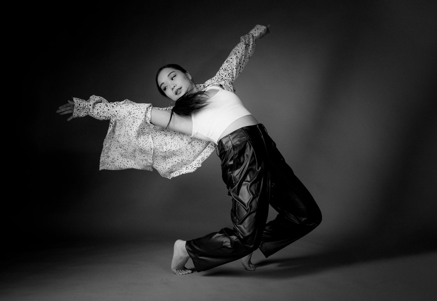 A dramatic black and white photo of a dancer performing in flowing garments with arms outstretched against a dark backdrop.