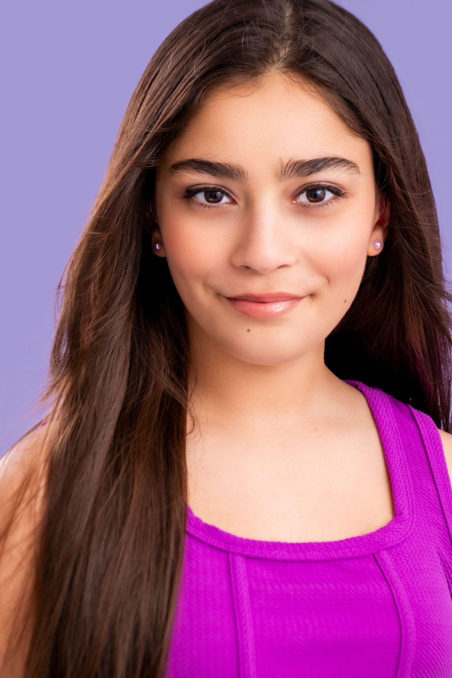 Close-up portrait of someone with long dark hair smiling warmly while wearing a bright magenta tank top against a purple background.
