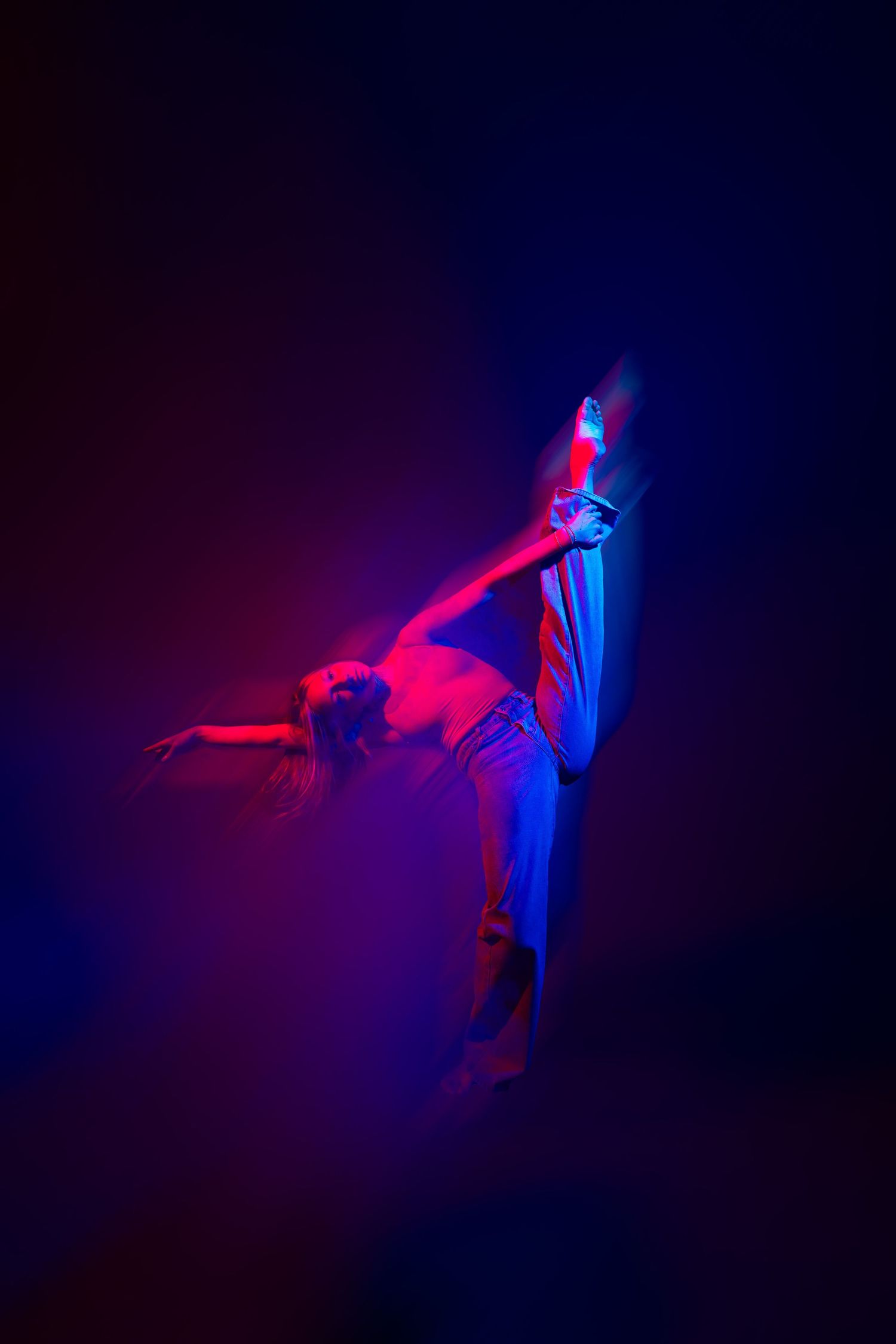 Dancer performs dynamic pose bathed in dramatic red and blue lighting against dark background.