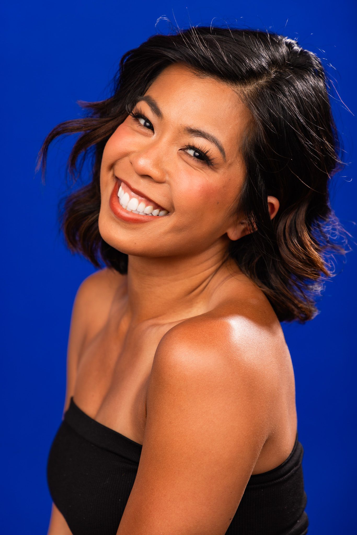 Person with wavy dark hair poses while smiling warmly against a vibrant blue background.