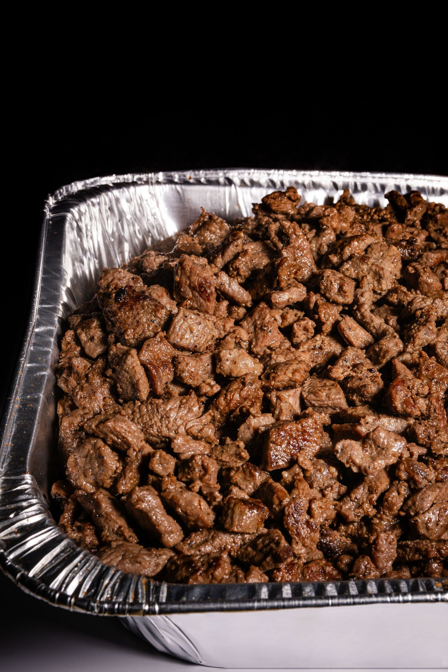Crumbled chocolate cookie mixture in an aluminum foil baking pan on a dark background.